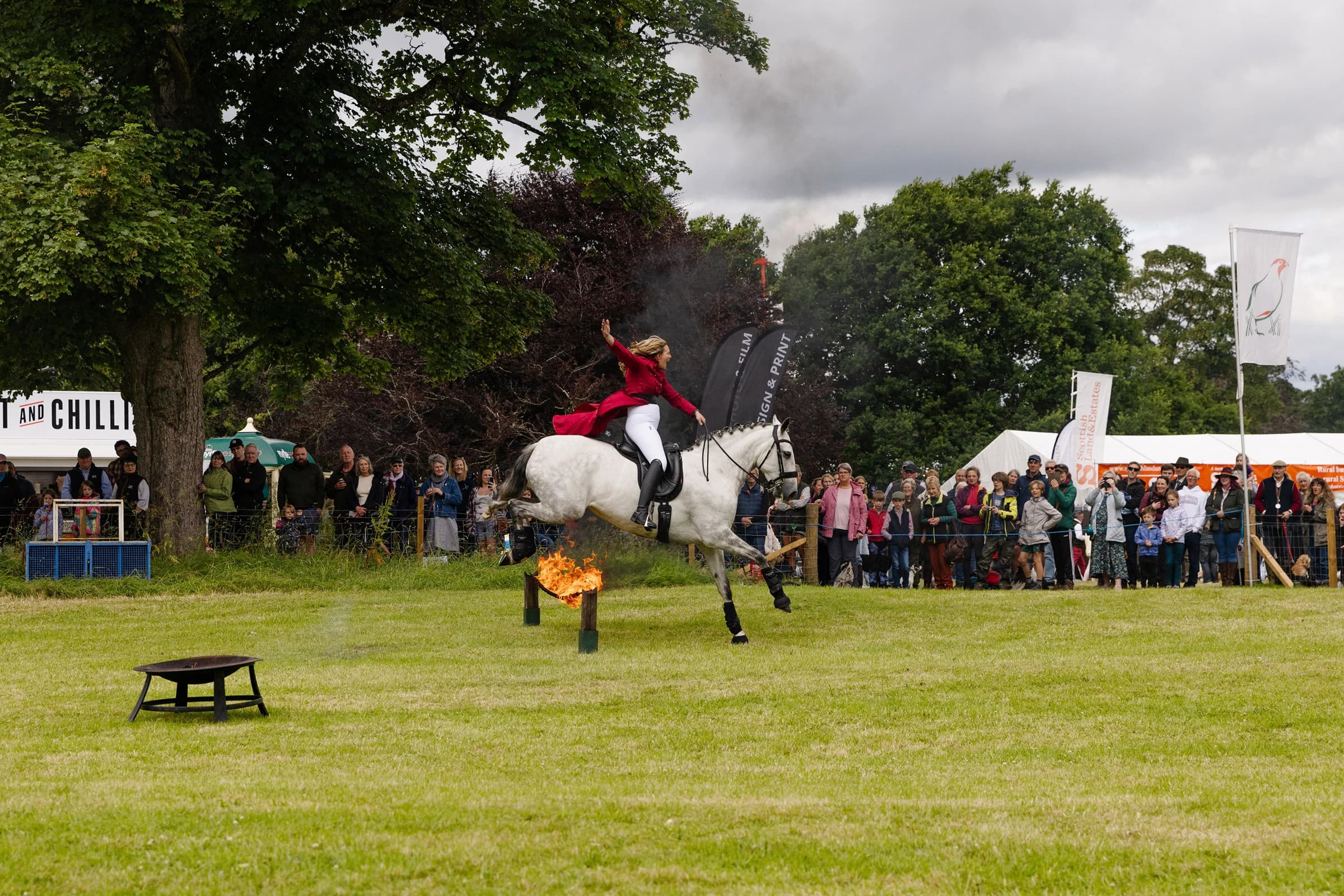 Woman riding horse jumping over flaming jump